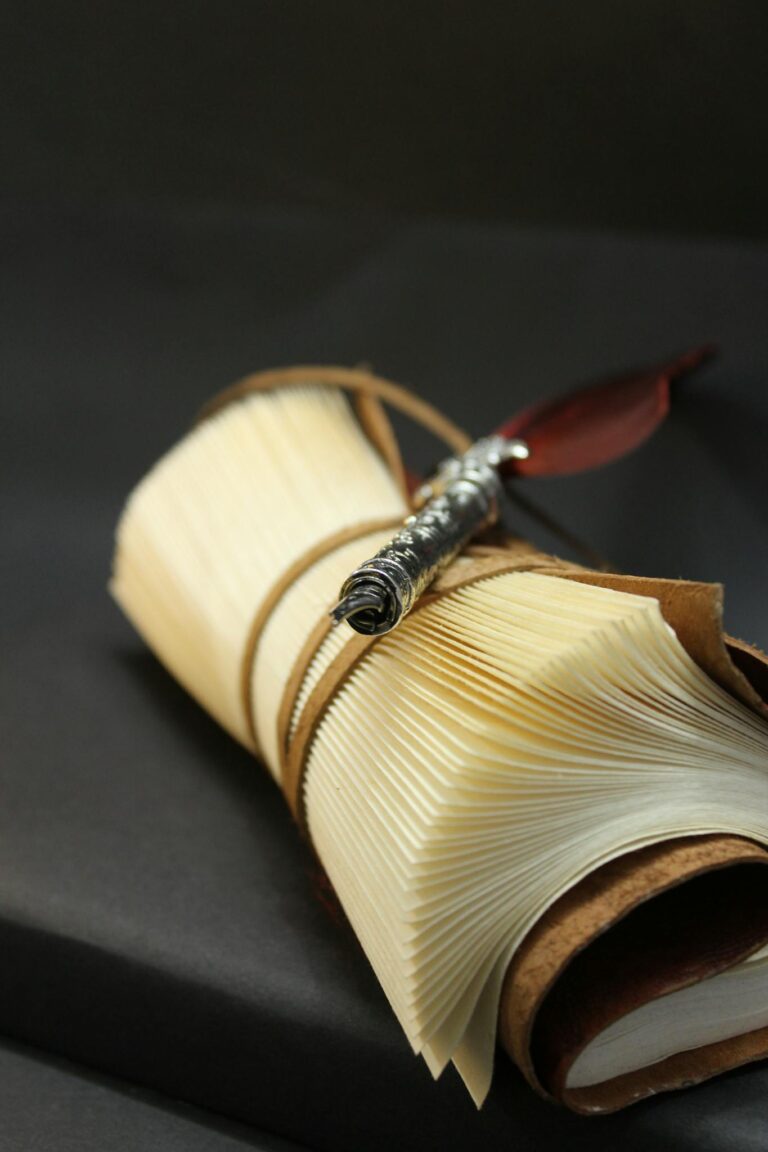 A close-up of a vintage leather notebook with an elegant silver pen on dark background.
