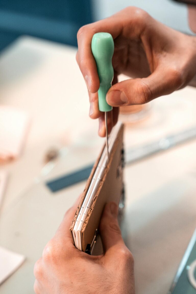 Hands performing detailed bookbinding with thread and awl, showcasing craftsmanship.